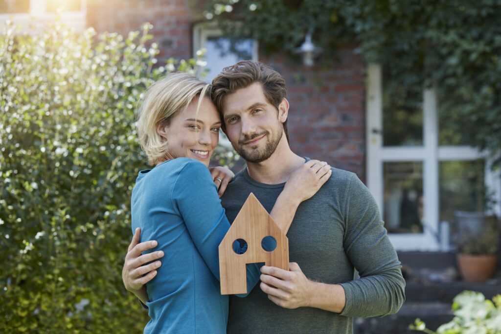Portrait of happy couple in front of their home with house model